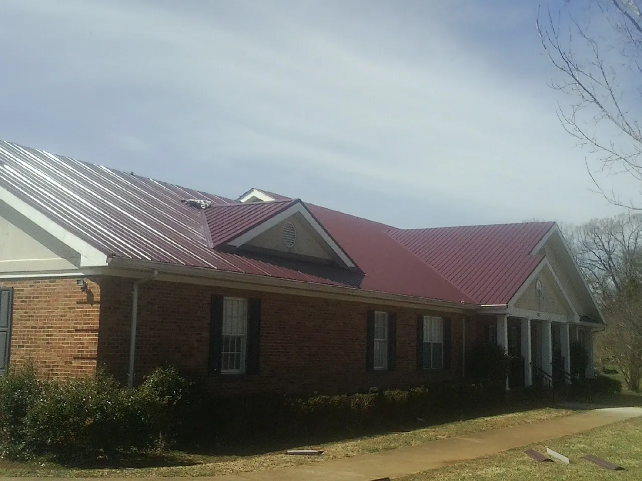 Red metal roof with gabled entries on a long brick building, from a Hail Damage Roof Repair job in Newcastle