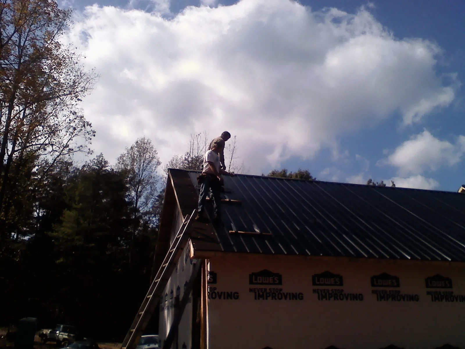 Roofer fastening dark metal panels high against a cloudy sky, from a Roof Inspection job in Newcastle