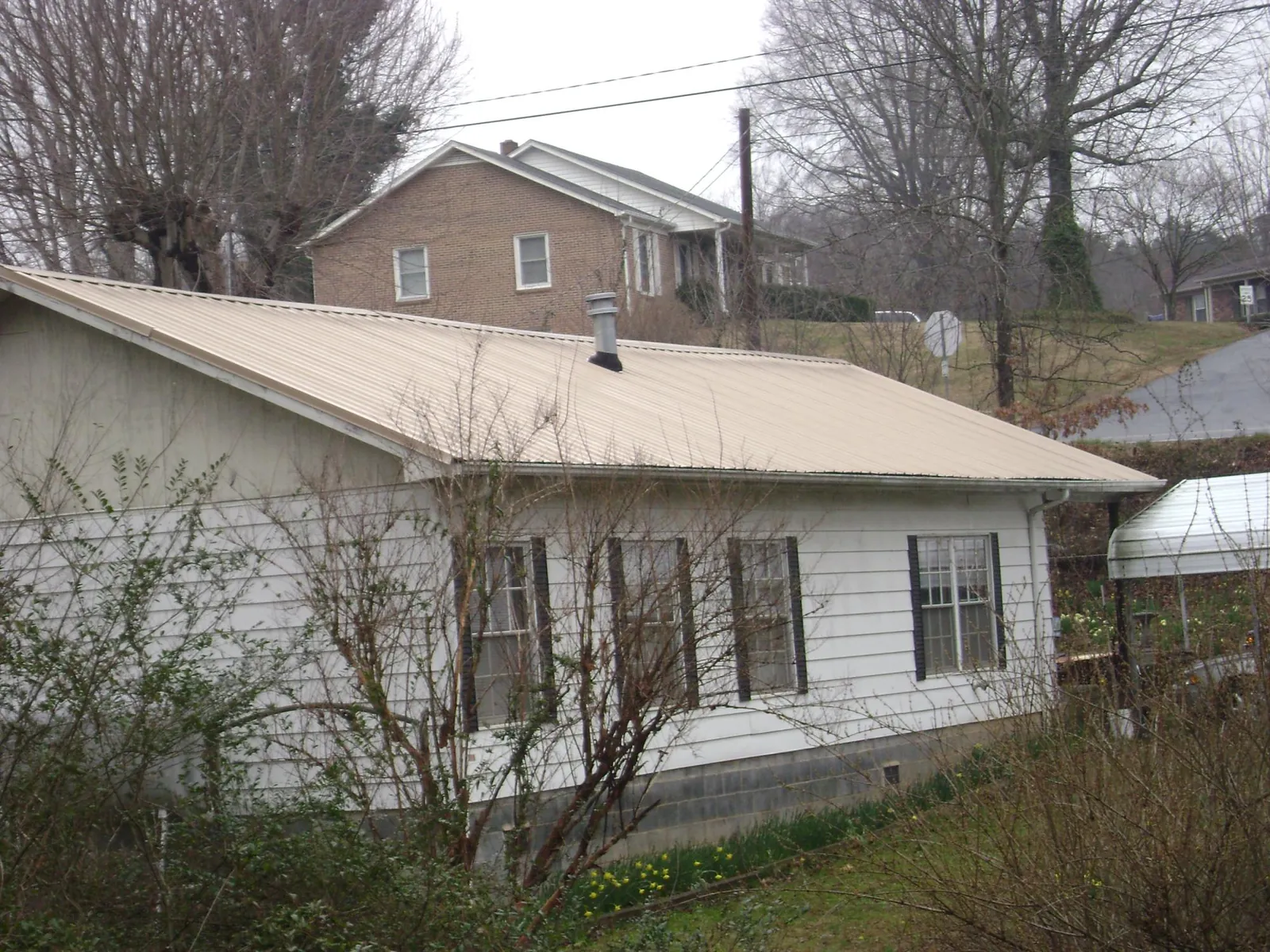 Tan metal roof on a white sided house set into a hillside — Commercial Roofing by Roofing Brothers in Newcastle